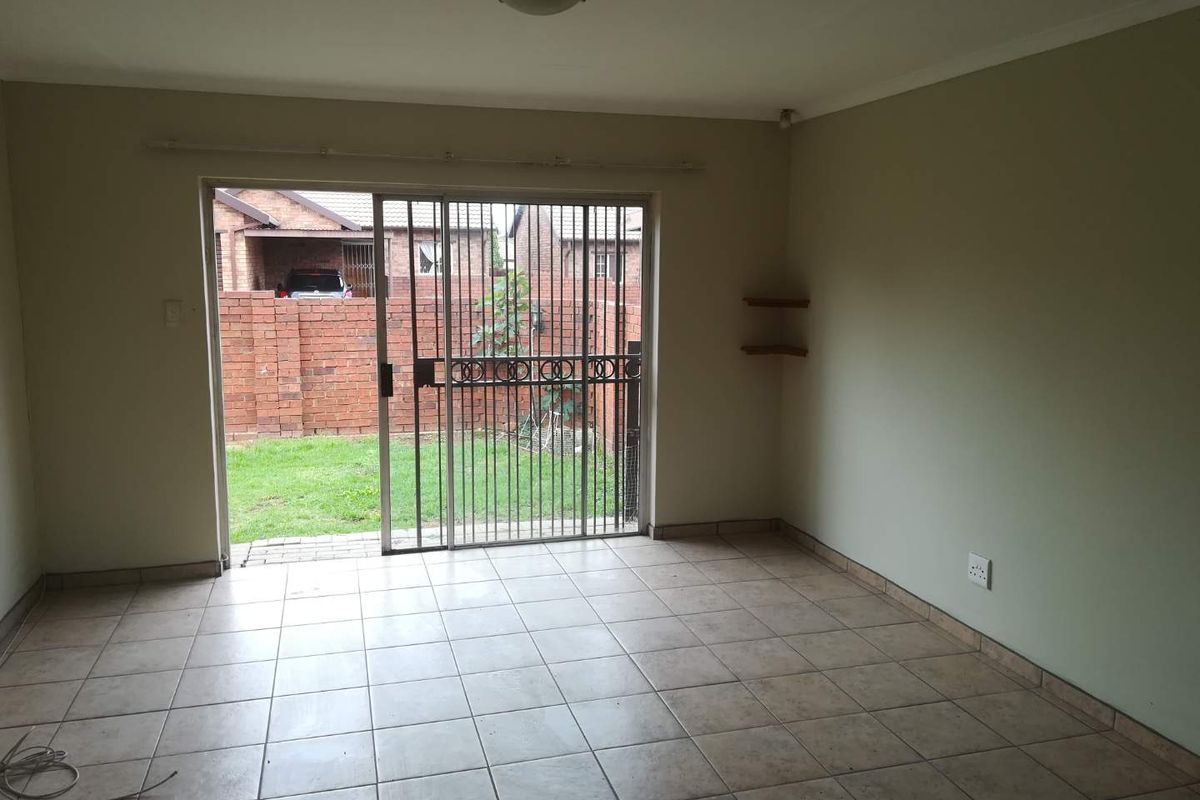An empty living room featuring ceramic floor tiles and a sliding glass door with a security gate, providing direct access to the rear garden.