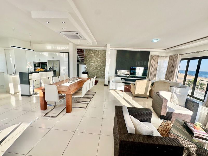 Spacious open-plan living, dining, and kitchen area featuring high-gloss cabinetry, stone feature wall, recessed lighting, and seamless access to the outdoor patio and sea view.