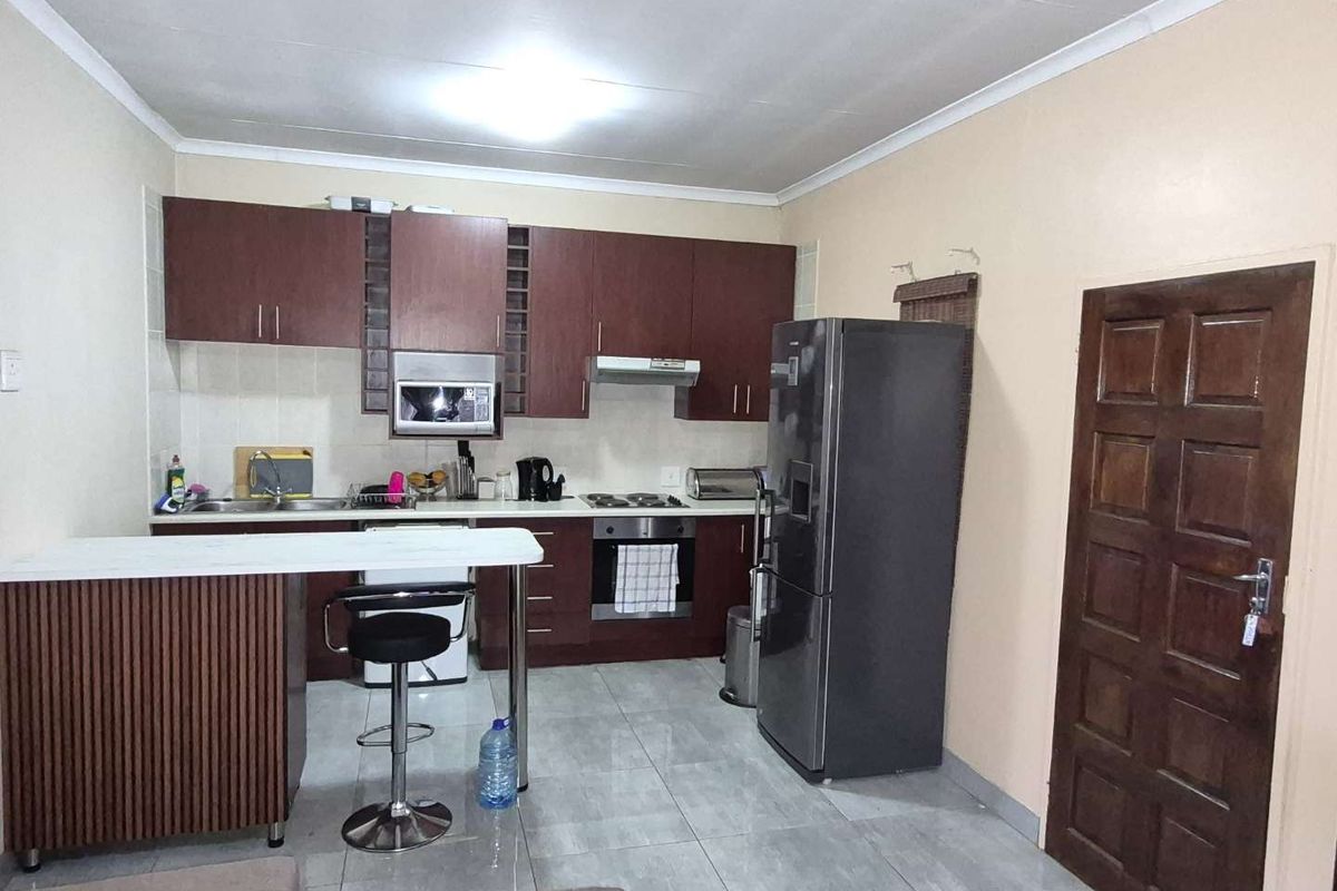 Functional kitchen featuring dark wood cabinetry, built-in oven and hob, breakfast bar, and tiled flooring, offering a practical layout for daily use.