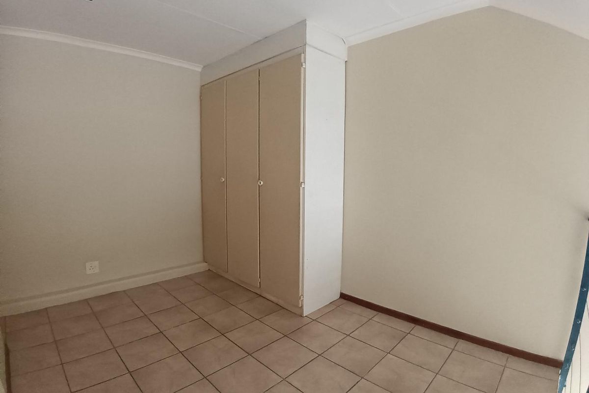 A vacant bedroom featuring neutral tiled flooring and a built-in wardrobe with ample storage space.