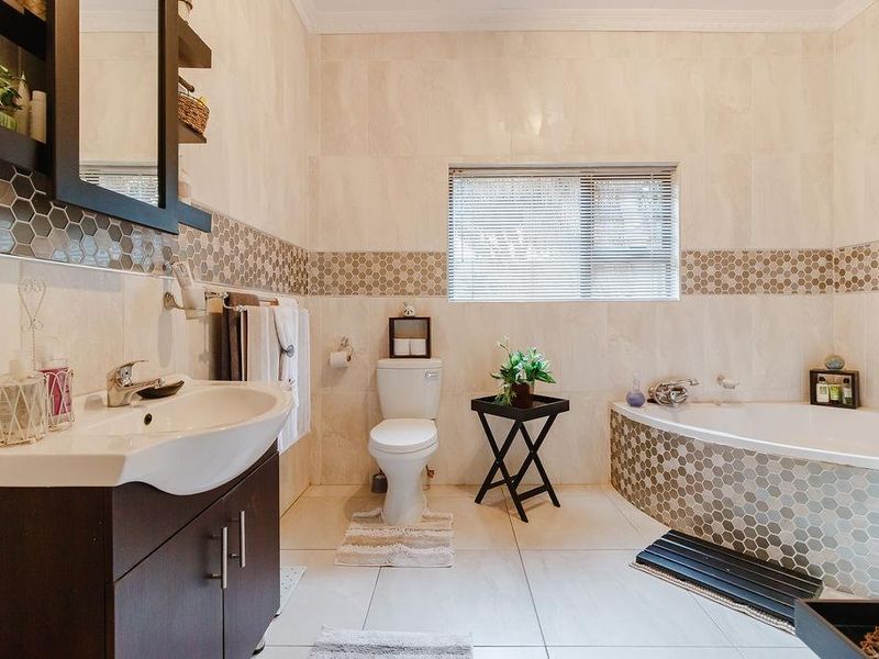 A well-maintained bathroom featuring a corner bathtub, vanity cabinet with basin, and neutral wall tiling with a decorative mosaic border.