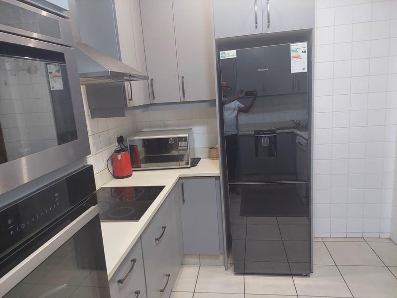 Modern kitchen featuring grey cabinetry, built-in oven, induction hob, extractor fan, and tiled splashback with neutral floor tiles.