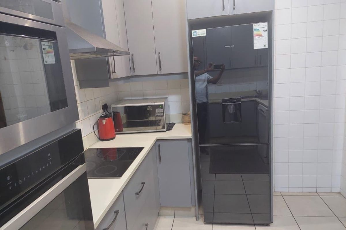 Modern kitchen featuring grey cabinetry, built-in oven, induction hob, extractor fan, and tiled splashback with neutral floor tiles.