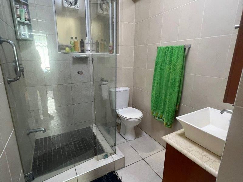 A functional bathroom featuring a glass-enclosed shower, vessel sink vanity, and neutral wall tiling, providing a practical layout for daily use.