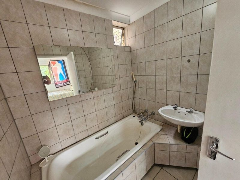 A dated bathroom featuring a built-in bathtub, wall-mounted basin, and full-height wall tiling, requiring cosmetic updates to modernize the space.