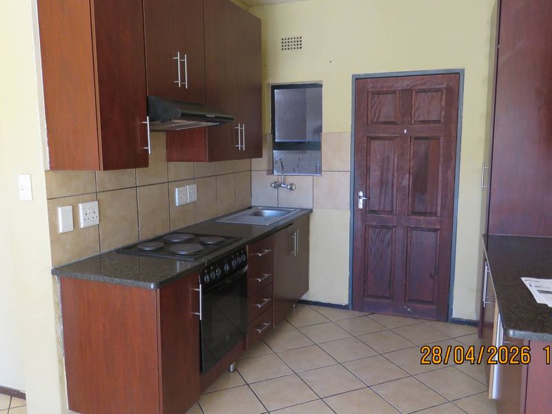 A functional kitchen featuring dark wood cabinetry, granite countertops, built-in oven and hob, and tiled flooring.