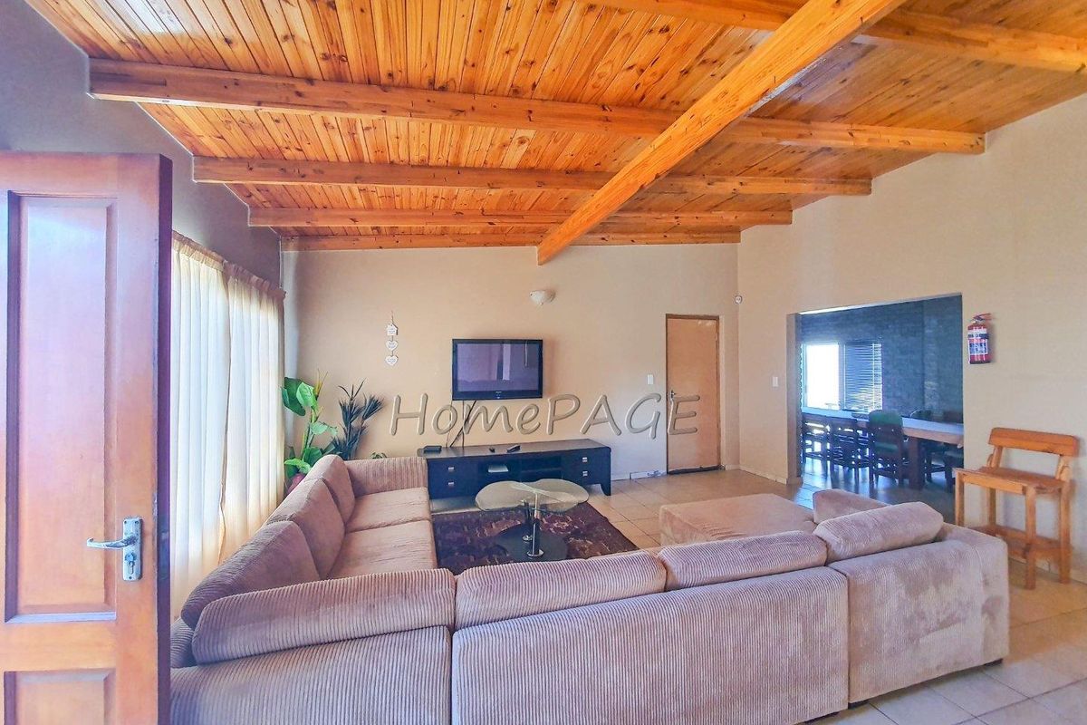 Spacious living area featuring exposed timber beam ceilings, tiled flooring, and an open-plan layout connecting to the adjacent dining space.