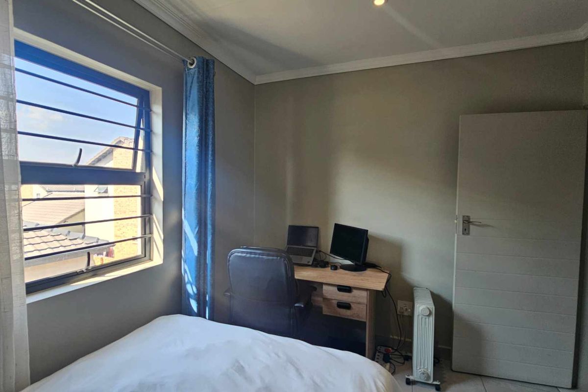 A functional bedroom featuring tiled flooring, cornice detailing, and a window fitted with security bars.