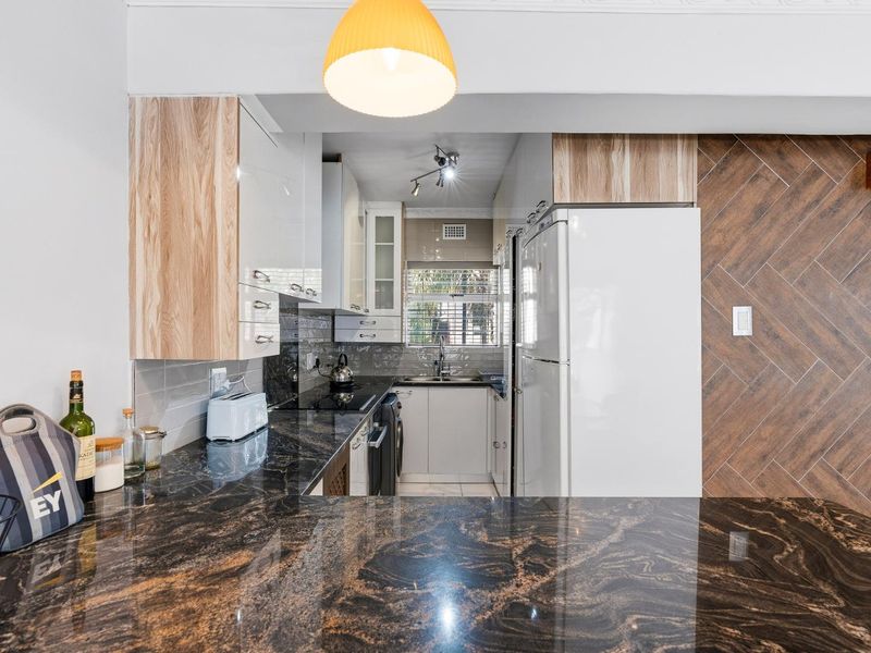 Modern kitchen featuring dark granite countertops, light wood-tone cabinetry, a stylish herringbone feature wall, and a functional layout with integrated storage.