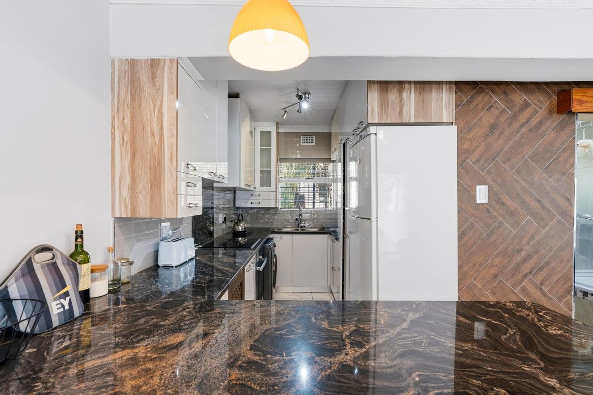 Modern kitchen featuring dark granite countertops, light wood-tone cabinetry, a stylish herringbone feature wall, and a functional layout with integrated storage.