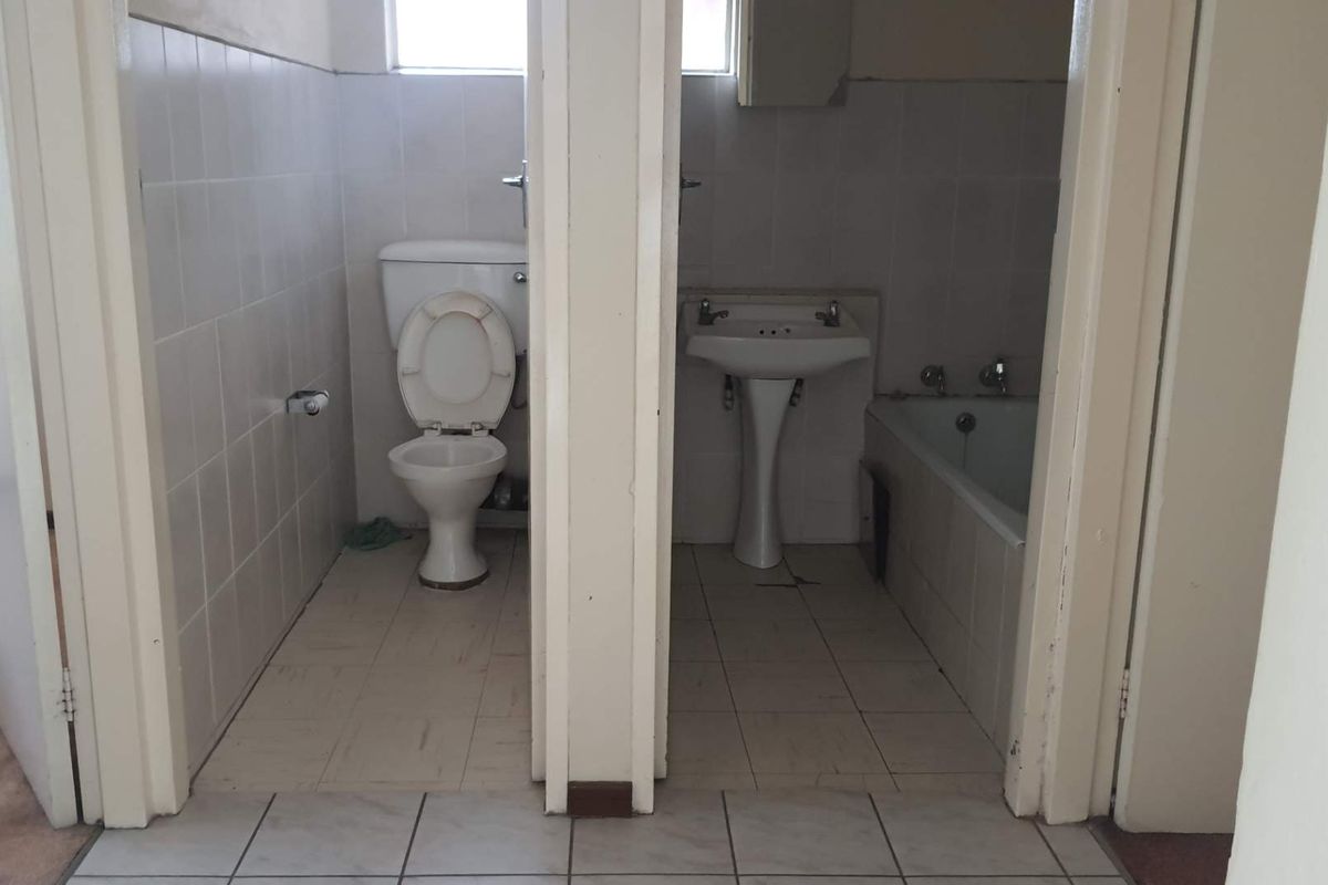 A dated bathroom featuring a separate toilet cubicle and a combined basin and bathtub area with ceramic tiling throughout.