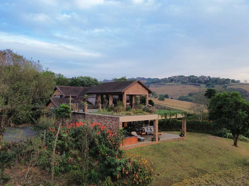 Aerial view of a multi-level brick residence featuring a covered patio, landscaped grounds, and expansive rural views.