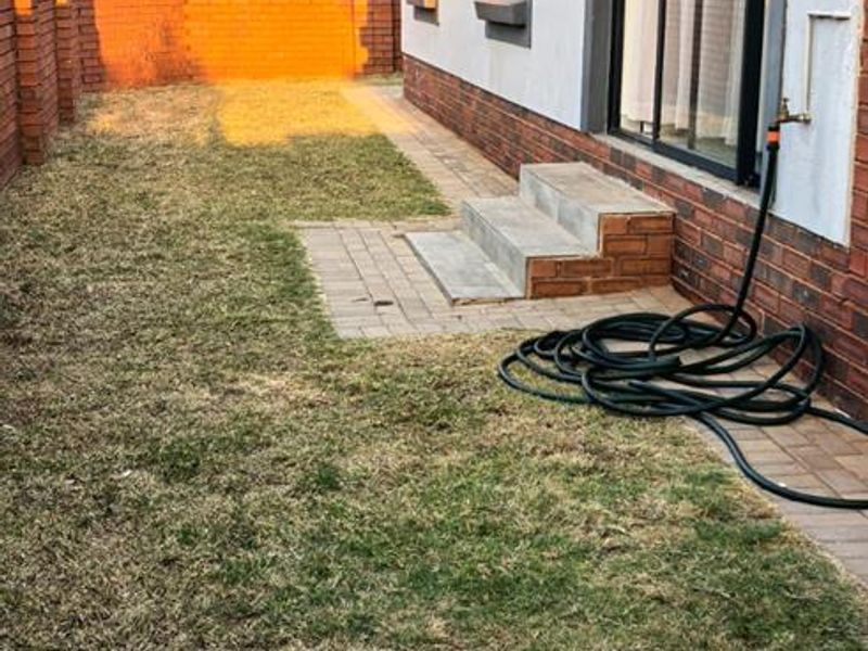 Rear exterior view of the apartment featuring a paved walkway, concrete steps, sliding glass door access, and a private garden area with brick boundary walls.