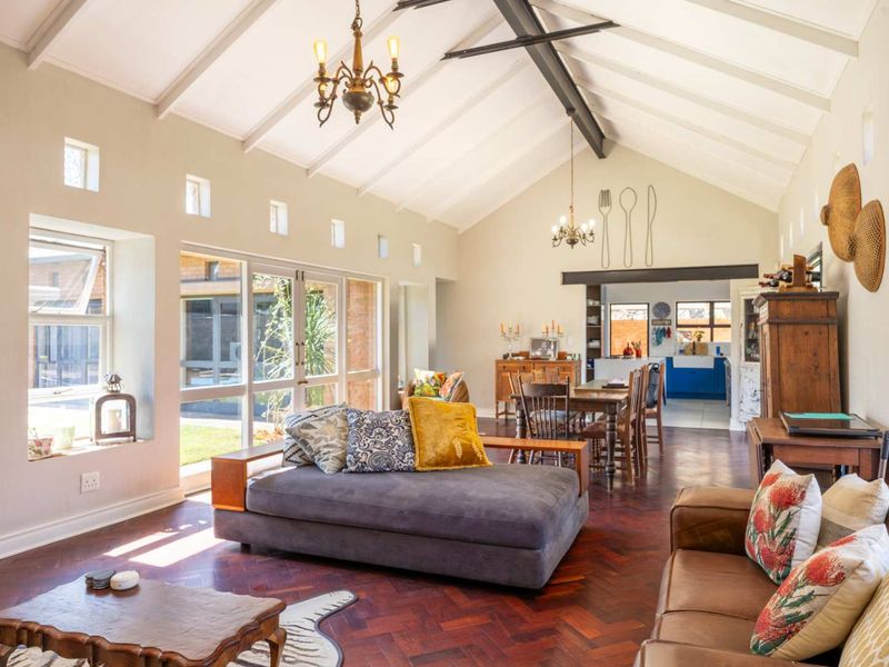 Spacious open-plan living and dining area featuring a high vaulted ceiling with exposed beams, rich herringbone parquet flooring, and large windows overlooking the garden.