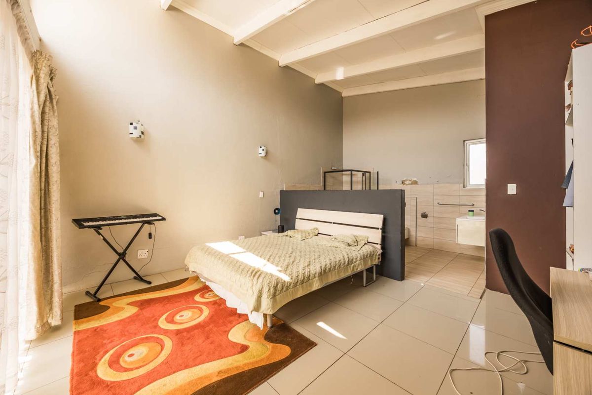 Spacious bedroom featuring exposed ceiling beams, tiled flooring, and an integrated vanity area with a partition wall.