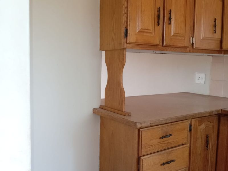 A dated kitchen area featuring traditional wooden cabinetry, laminate countertops, and tiled flooring, offering potential for a modern renovation.