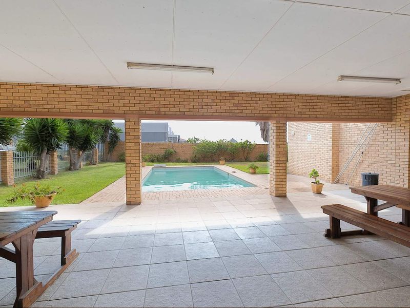A covered outdoor patio area featuring tiled flooring and brick pillars, overlooking a private swimming pool and garden space.