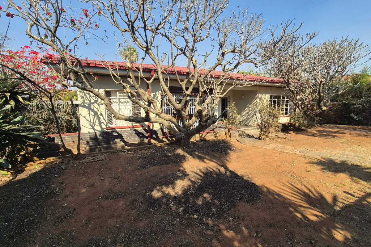 Rear view of a single-story house featuring a tiled roof, brick facade, and security bars on the windows, set within a large unlandscaped garden.