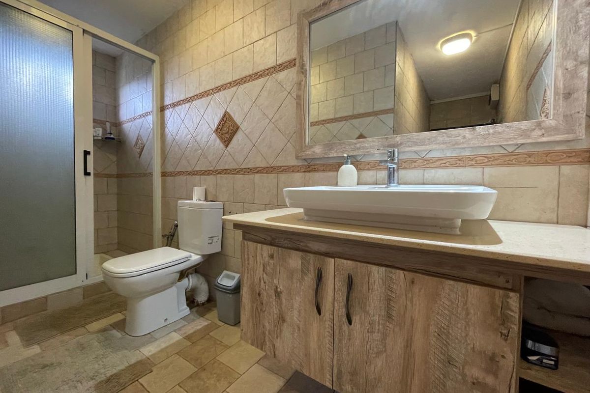 A functional bathroom featuring a wood-finish vanity with a vessel sink, a framed wall mirror, tiled walls, and a separate shower enclosure.