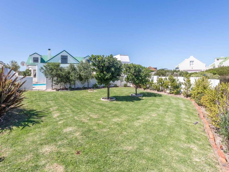 A well-maintained garden featuring a manicured lawn, established trees, and brick-edged garden beds, with a view toward the rear of the house and pool.