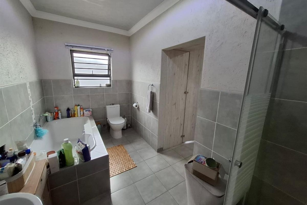 A functional bathroom featuring a built-in bathtub, a separate glass-enclosed shower, and neutral tiled finishes throughout.