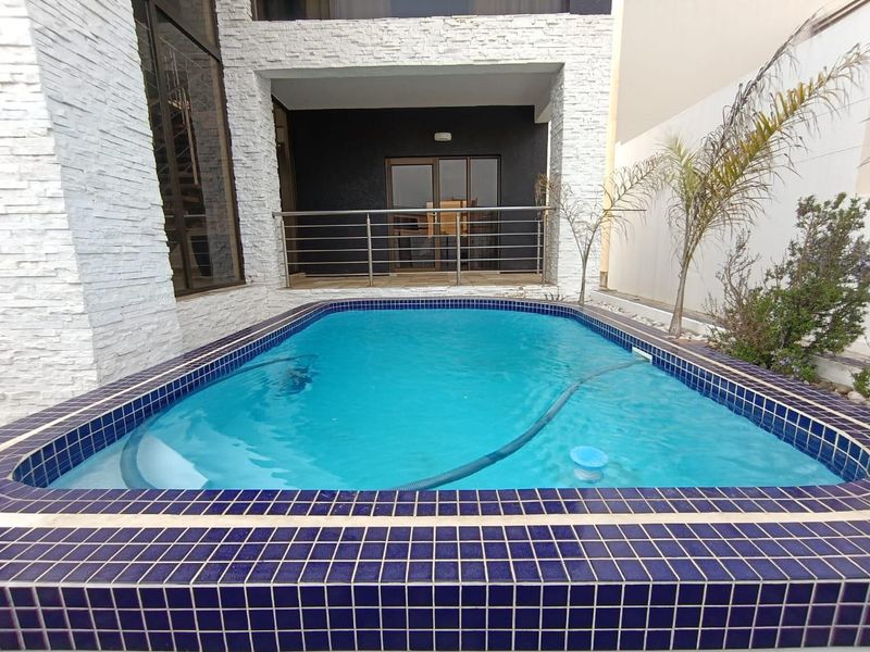 A modern outdoor pool area featuring a tiled swimming pool, stainless steel balustrade, and striking stacked stone exterior wall cladding.