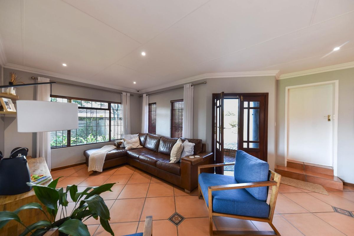 A bright living room featuring terracotta floor tiles, recessed downlighting, and direct access to the exterior through a timber-framed glass door.