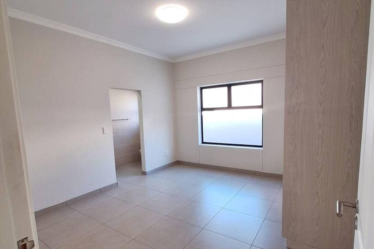 A bright, empty bedroom featuring neutral floor tiles, built-in wooden cabinetry, and an adjoining en-suite bathroom.
