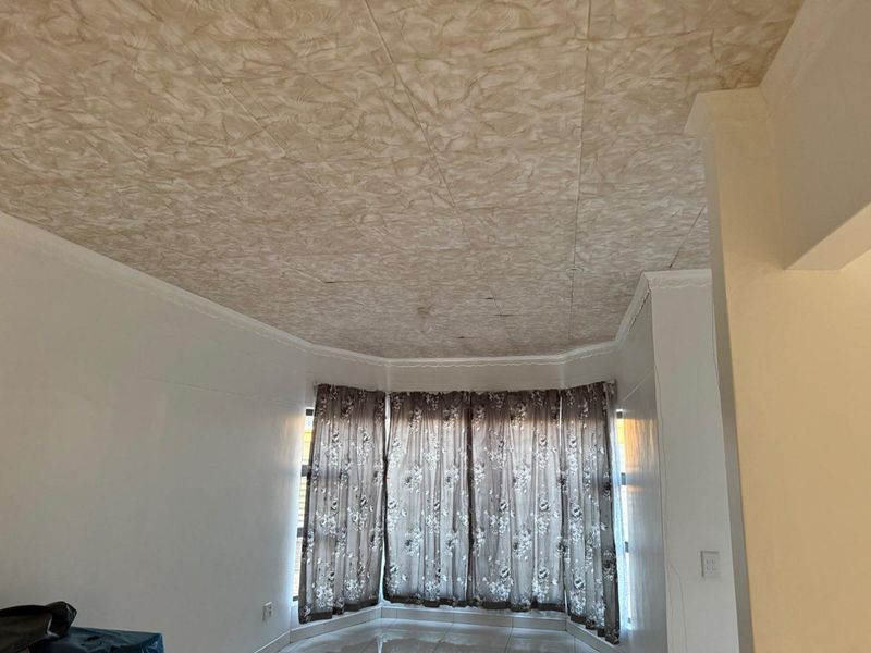 An empty living room featuring a bay window, tiled flooring, and a textured ceiling. The space requires cosmetic updates to improve its overall condition.