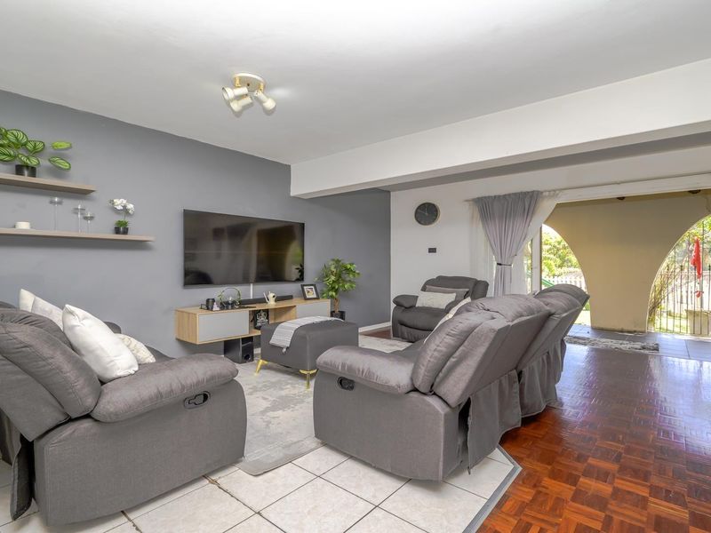 Spacious living room featuring a mix of tiled and parquet flooring, floating wall shelves, and direct access to an outdoor patio area.