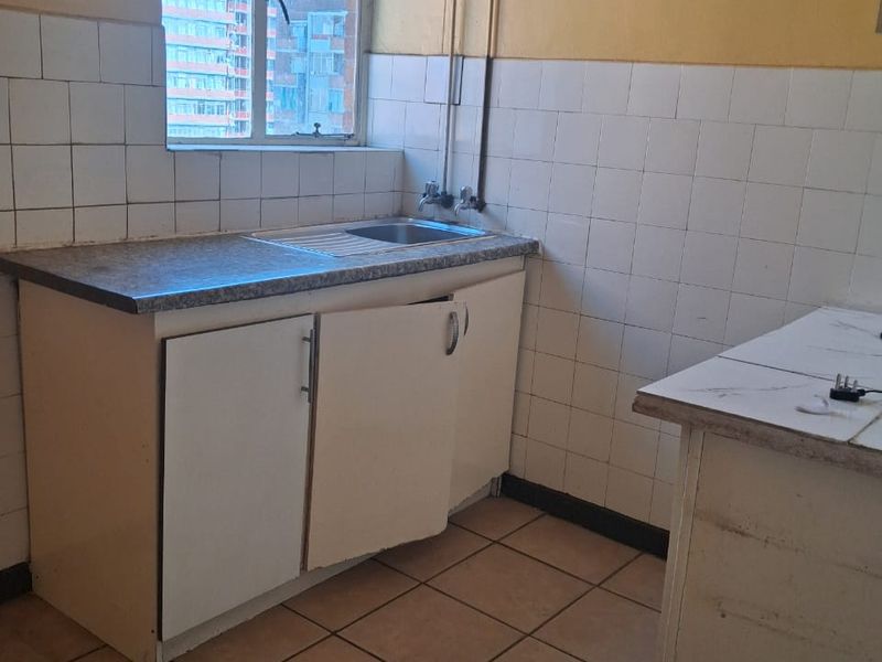 A dated kitchen area featuring tiled walls, a stainless steel sink, and built-in cabinetry in need of repair and modernization.