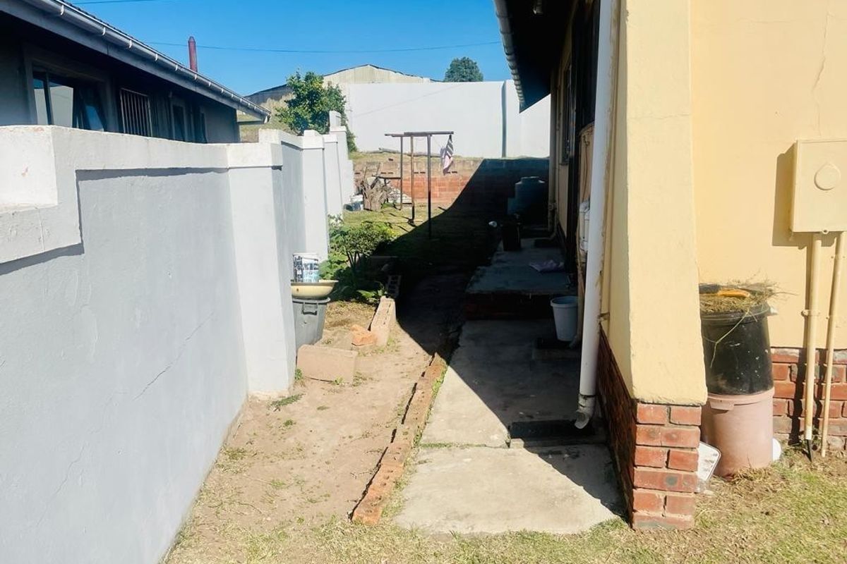 A narrow rear exterior side passage featuring a concrete walkway, boundary wall, and brick foundation detailing along the side of the house.