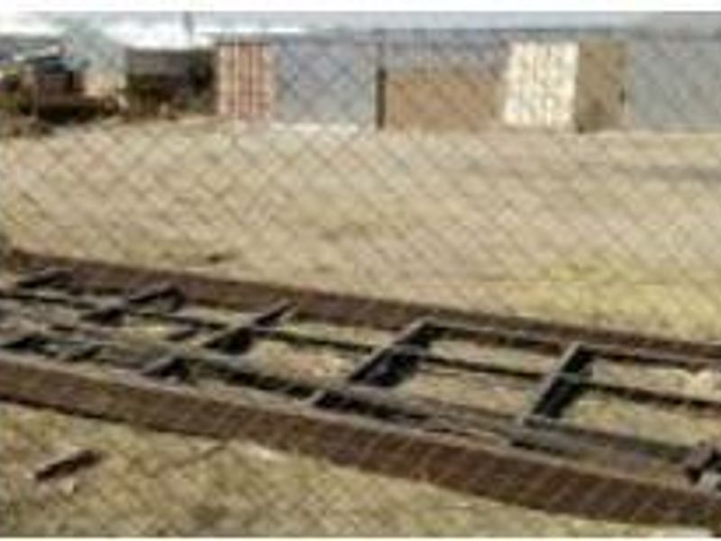 An industrial outdoor area featuring a chain-link fence and a metal frame structure on unimproved ground.