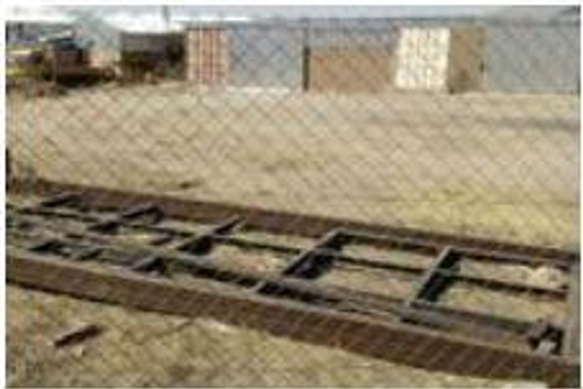 An industrial outdoor area featuring a chain-link fence and a metal frame structure on unimproved ground.