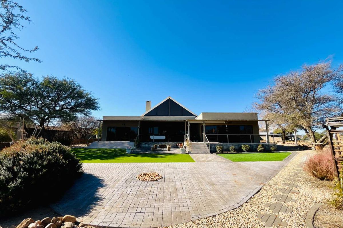 Rear view of the house featuring a paved patio area, manicured lawn, and covered veranda with large glass sliding doors.