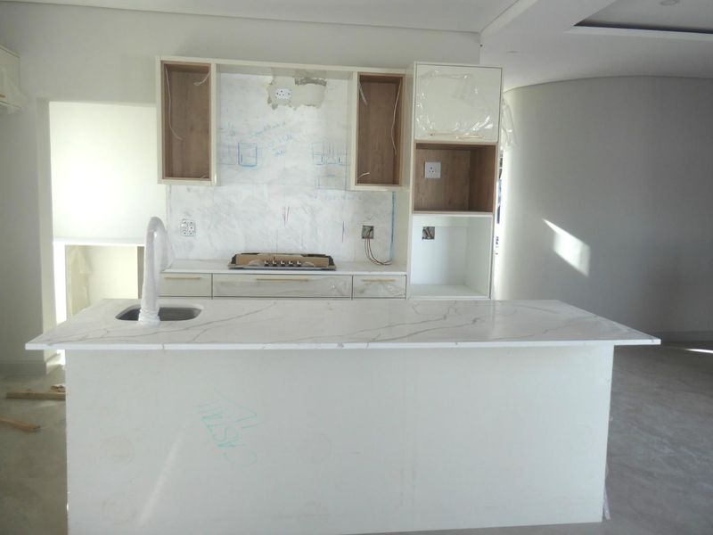 An unfinished modern kitchen featuring a central island with stone countertops, built-in hob, and cabinetry in the process of installation.