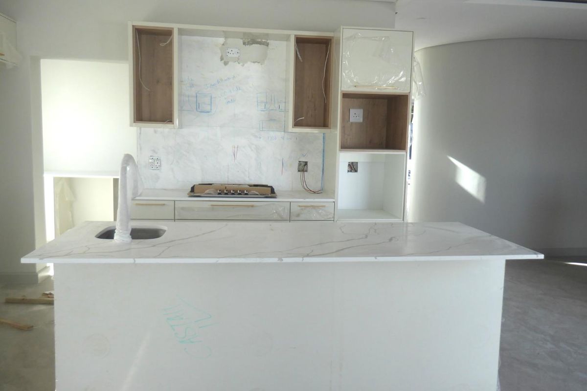 An unfinished modern kitchen featuring a central island with stone countertops, built-in hob, and cabinetry in the process of installation.