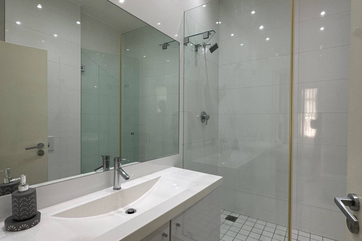 Modern bathroom featuring a sleek vanity with integrated basin, large wall mirror, and a walk-in shower with glass enclosure and gold-toned trim.