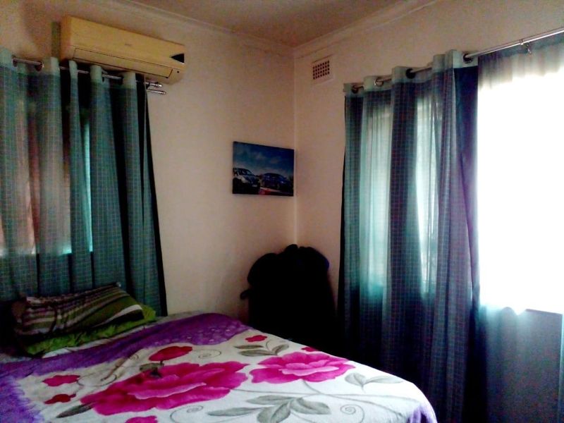 A bedroom featuring a wall-mounted split-system air conditioner and dual window treatments.