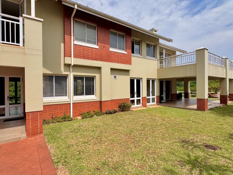 Rear view of the house featuring a spacious tiled patio, upper-level balcony, brick and plaster facade, and well-maintained garden area.
