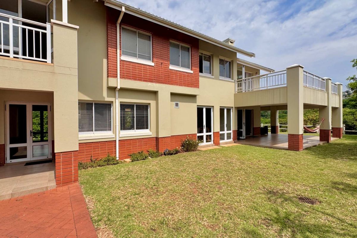 Rear view of the house featuring a spacious tiled patio, upper-level balcony, brick and plaster facade, and well-maintained garden area.