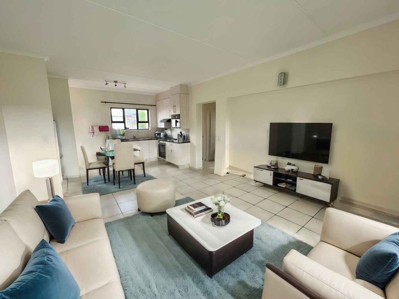 An open-plan living and dining area featuring tiled flooring and a modern kitchen with built-in cabinetry, oven, and hob.
