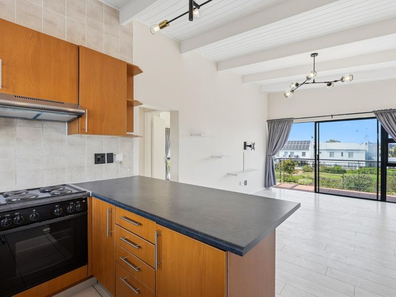 Open-plan kitchen and living area featuring wooden cabinetry, exposed ceiling beams, and a sliding door leading to a balcony with neighborhood views.