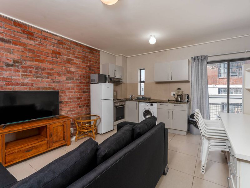 Open-plan living and kitchen area featuring an exposed brick feature wall, tiled flooring, and direct access to a balcony through sliding glass doors.