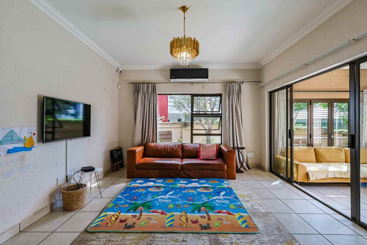 A bright living room featuring tiled flooring, a wall-mounted air conditioning unit, and large sliding glass doors that open onto an adjacent patio area.