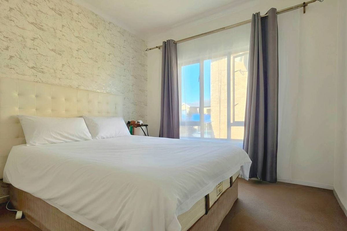 A bedroom featuring a textured accent wall, carpeted flooring, and a large window allowing natural light.