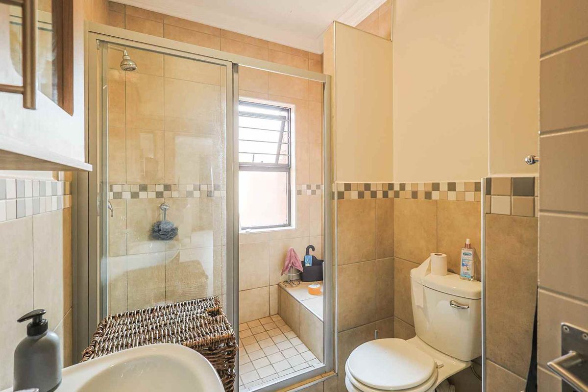A functional bathroom featuring a glass-enclosed shower, a built-in bathtub, a toilet, and a pedestal basin with neutral wall tiling.