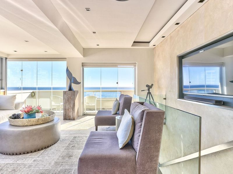 Modern living room featuring high-end finishes, recessed lighting, a glass balustrade, and expansive floor-to-ceiling glass doors offering panoramic ocean views.