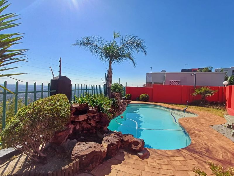 Outdoor pool area featuring a swimming pool, brick paving, and a rock feature, enclosed by a perimeter wall with electric fencing.