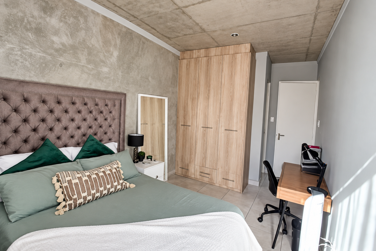 Modern bedroom featuring an exposed concrete ceiling, built-in wooden wardrobe, and neutral tiled flooring, offering a contemporary industrial aesthetic.